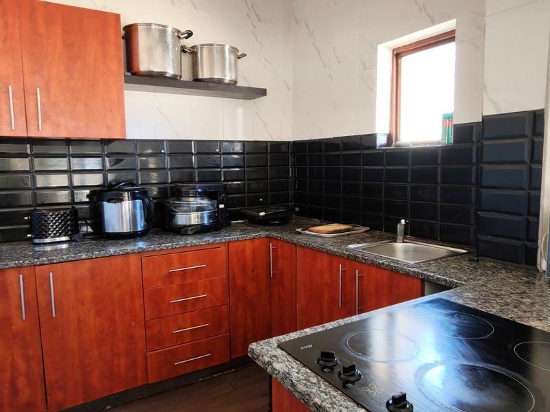 A functional kitchen featuring wood-finish cabinetry, granite countertops, a black subway tile backsplash, and a built-in electric hob.