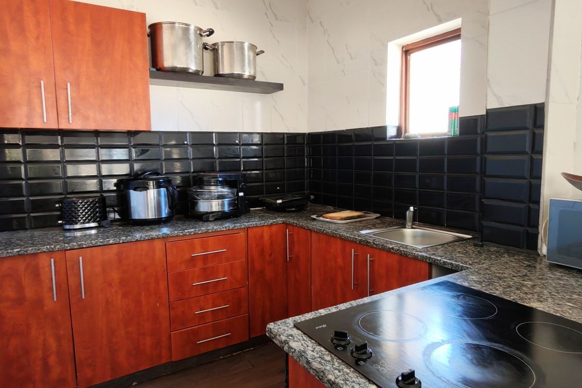 A functional kitchen featuring wood-finish cabinetry, granite countertops, a black subway tile backsplash, and a built-in electric hob.