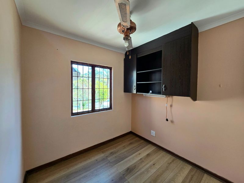 A compact bedroom featuring laminate flooring, a ceiling fan, and built-in wall cabinetry, offering a functional space ready for personalization.