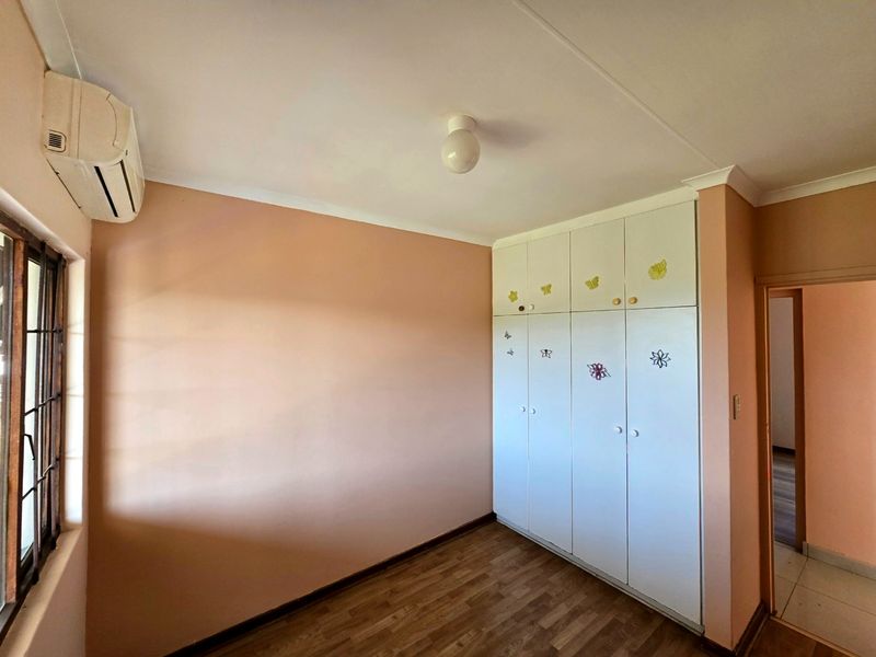 A bedroom featuring built-in cupboards, laminate flooring, and an installed air conditioning unit, providing a functional and ready-to-occupy space.
