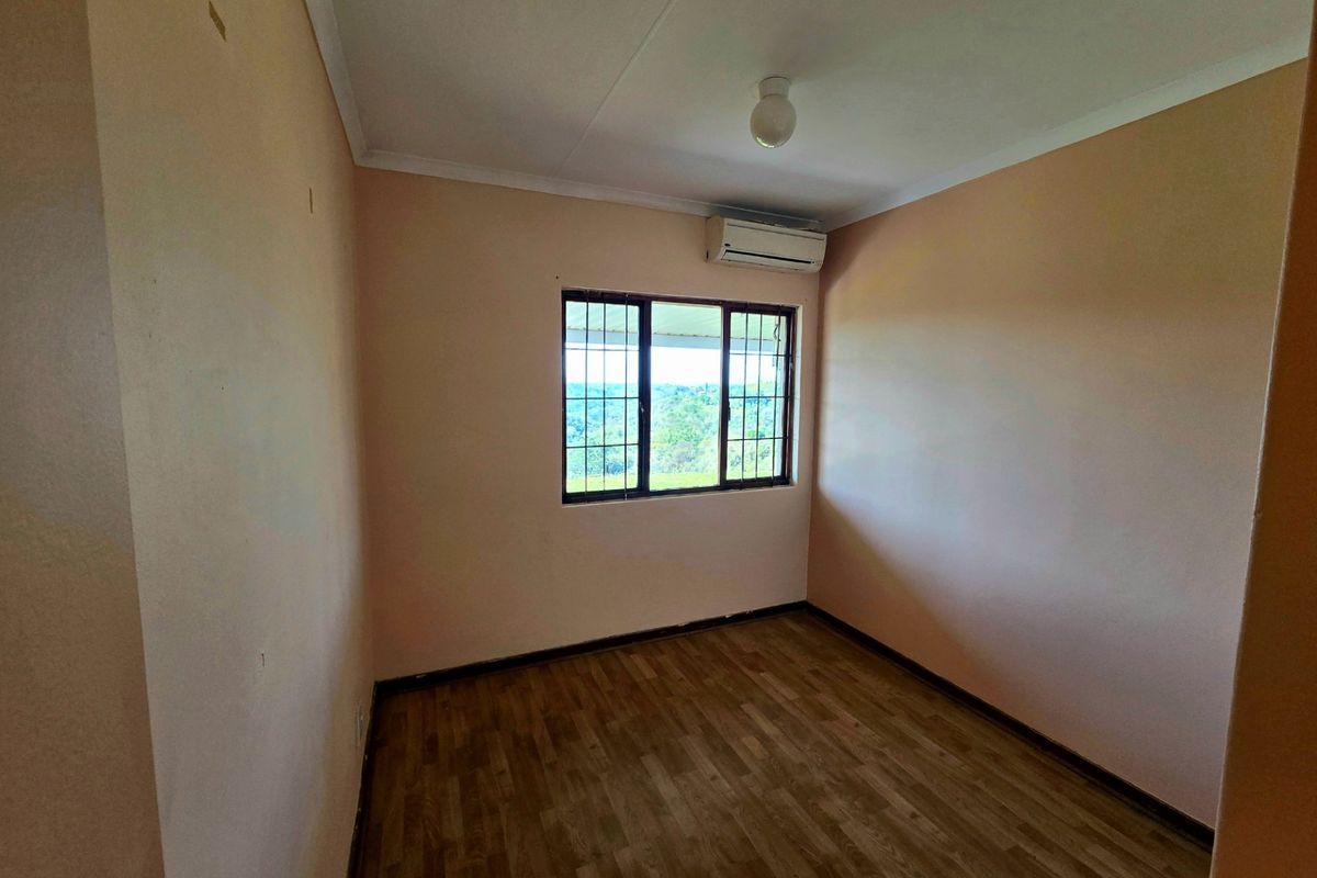 An empty bedroom featuring laminate flooring, a wall-mounted air conditioning unit, and security bars on the window.