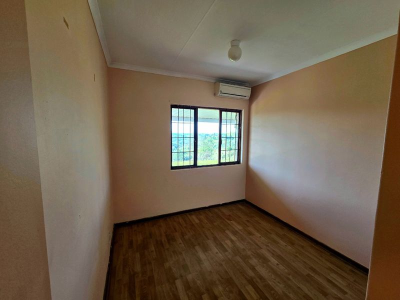 An empty bedroom featuring laminate flooring, a wall-mounted air conditioning unit, and security bars on the window.