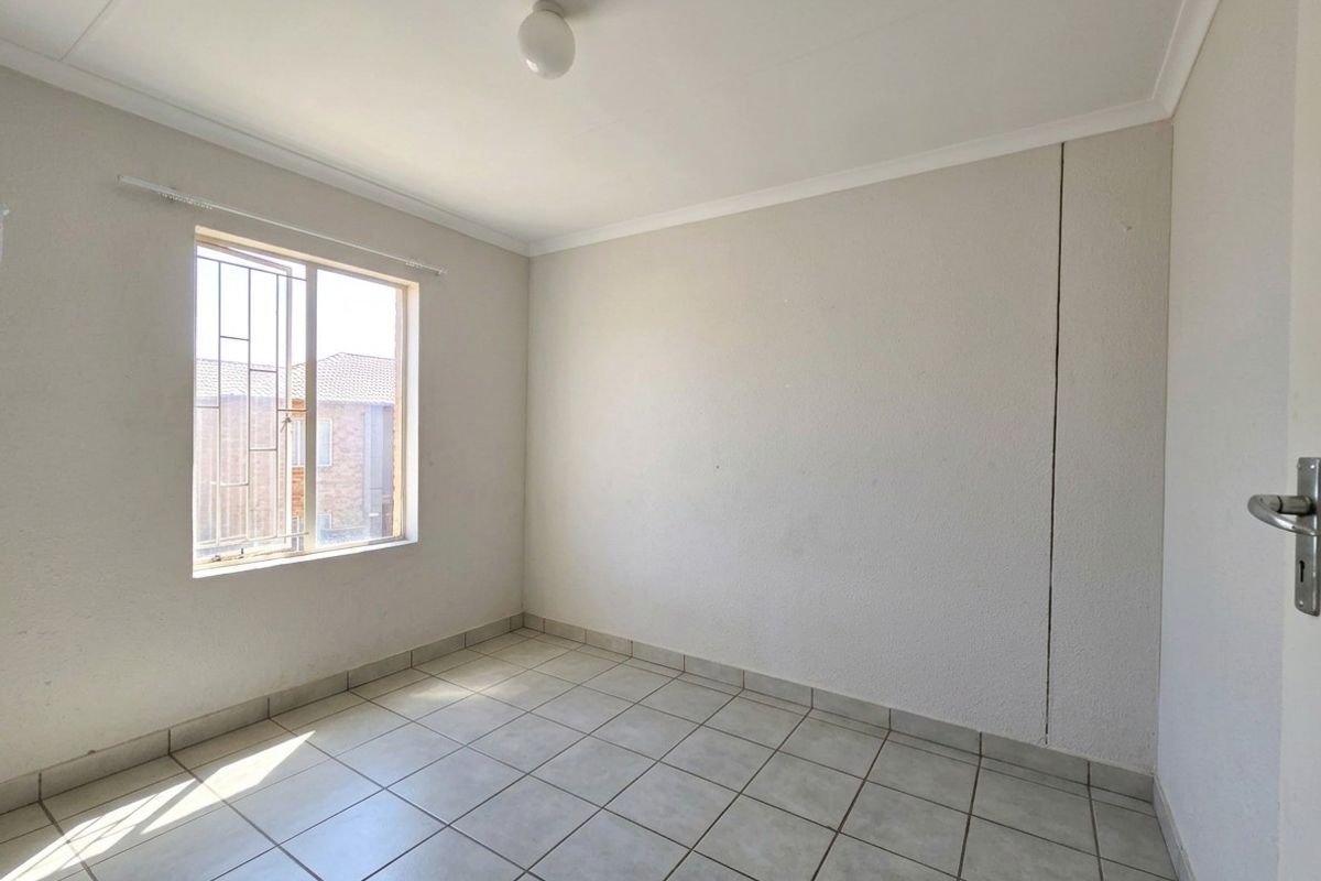 An empty bedroom featuring tiled flooring, a window with security bars, and a visible vertical crack on the wall.