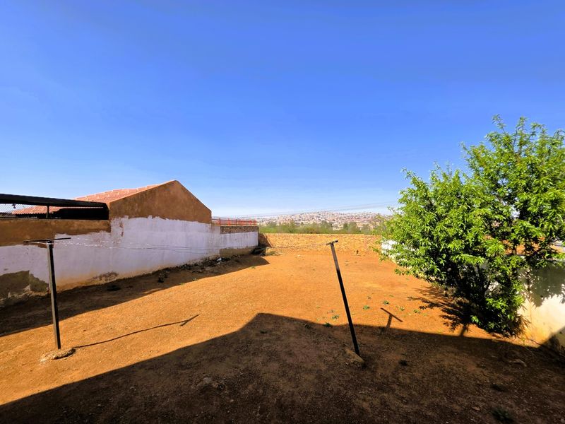 A spacious, undeveloped backyard area featuring perimeter walls and distant urban views, offering significant potential for landscaping and outdoor improvement.