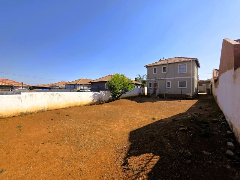 Rear view of a two-story house featuring a large, unlandscaped backyard enclosed by a perimeter wall.