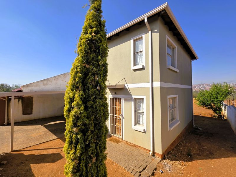 A two-story residential property featuring a paved driveway, attached carport, and secure entrance gate, set on a spacious plot.