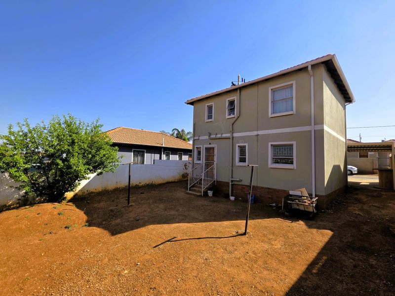 Rear view of a two-story house featuring a tiled roof, security bars on windows, and an unlandscaped garden area.