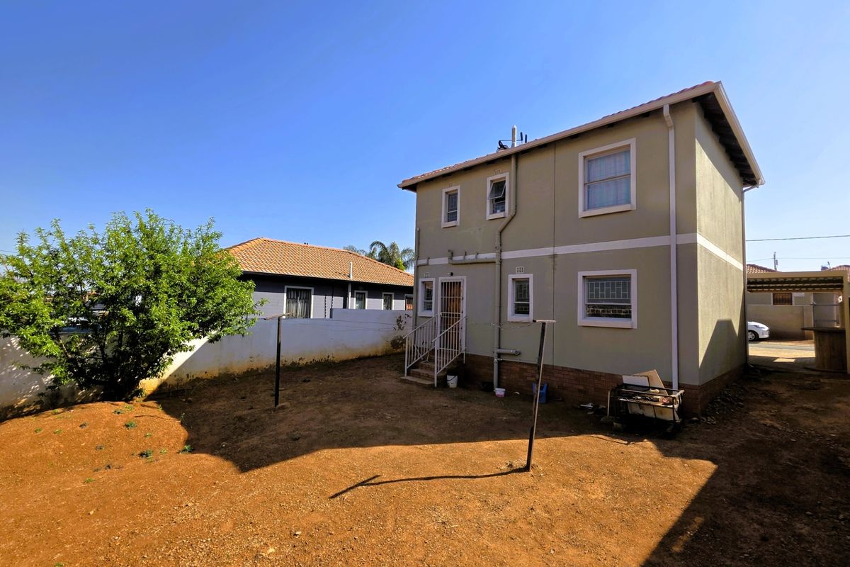 Rear view of a two-story house featuring a tiled roof, security bars on windows, and an unlandscaped garden area.