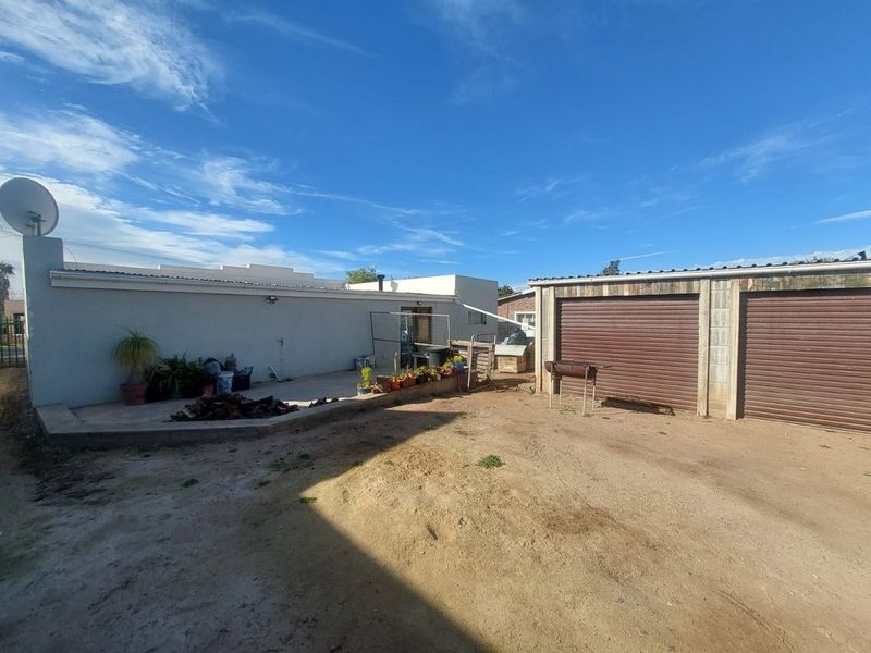 Rear exterior view featuring a concrete patio area and a double garage with roller shutter doors, set within an unpaved yard.