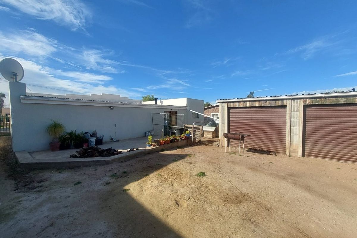 Rear exterior view featuring a concrete patio area and a double garage with roller shutter doors, set within an unpaved yard.