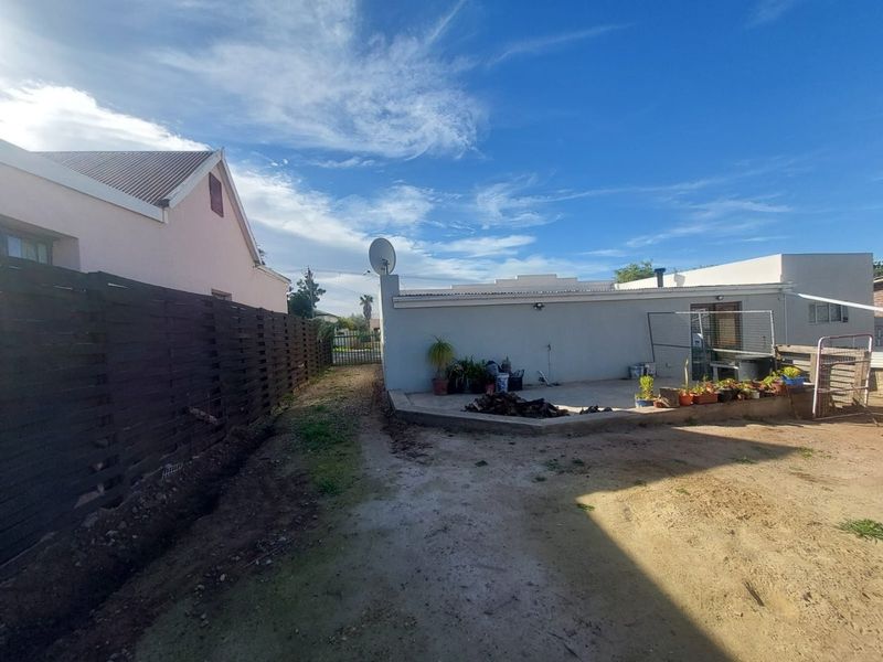 Rear exterior view of the property featuring a concrete patio area, timber boundary fencing, and a large open yard space.