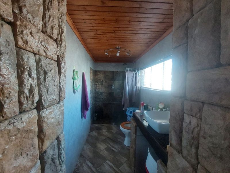 Bathroom featuring stone-clad walls, a timber ceiling, a vessel sink vanity, and a walk-in shower with dark tiling.