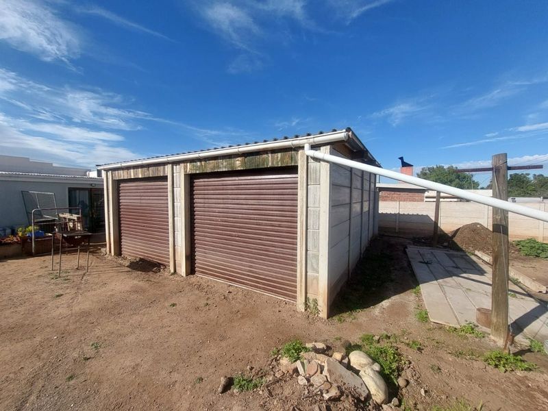 A detached double garage featuring roller doors and precast concrete walling, situated on an unpaved plot with basic guttering infrastructure.