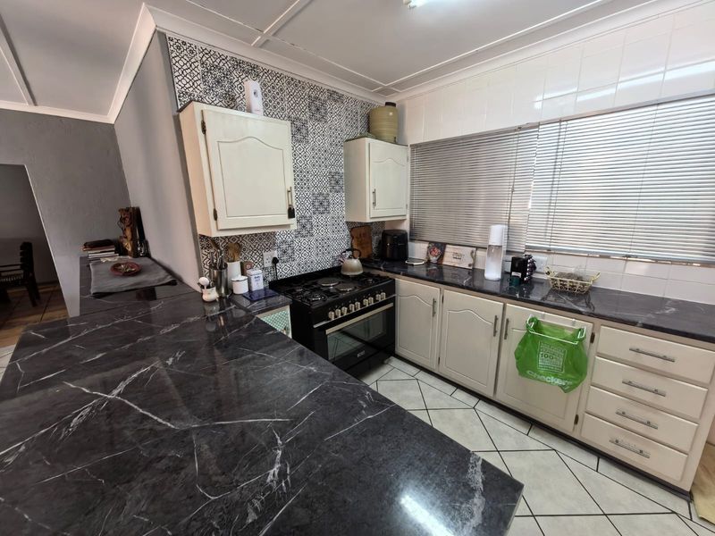 A functional kitchen featuring dark marble-look countertops, patterned tile backsplash, built-in cabinetry, and a gas stove with oven.