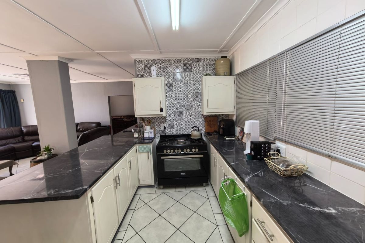 A functional kitchen featuring dark marble-look countertops, white cabinetry, a gas stove with oven, and decorative tiled splashback.