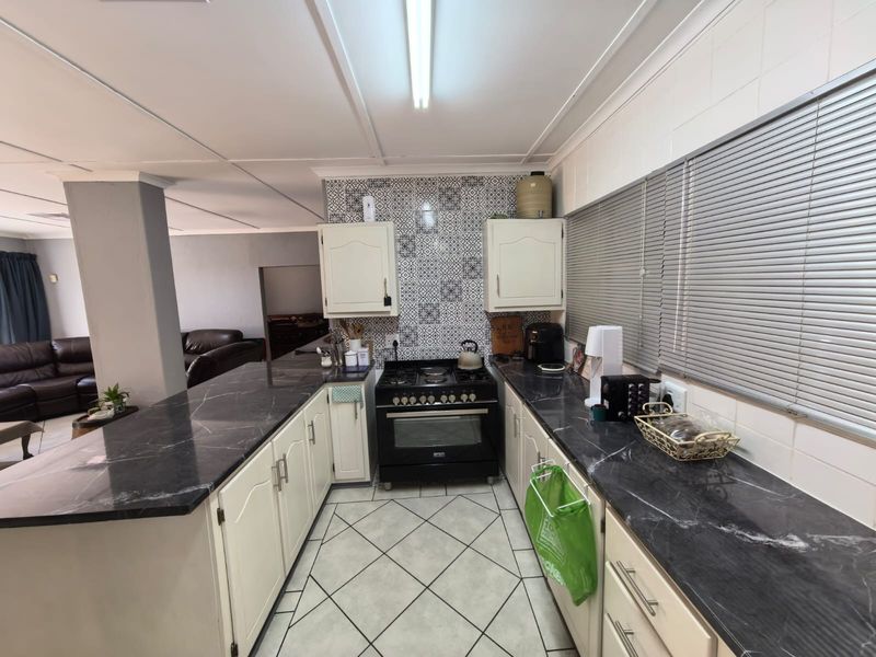 A functional kitchen featuring dark marble-look countertops, white cabinetry, a gas stove with oven, and decorative tiled splashback.