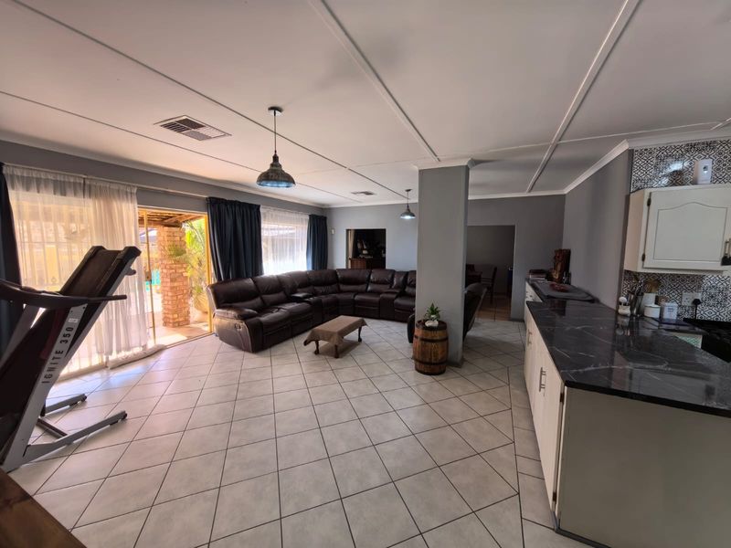 Spacious open-plan living area featuring tiled floors, a modern kitchen with stone countertops, and sliding glass doors leading to an outdoor patio.