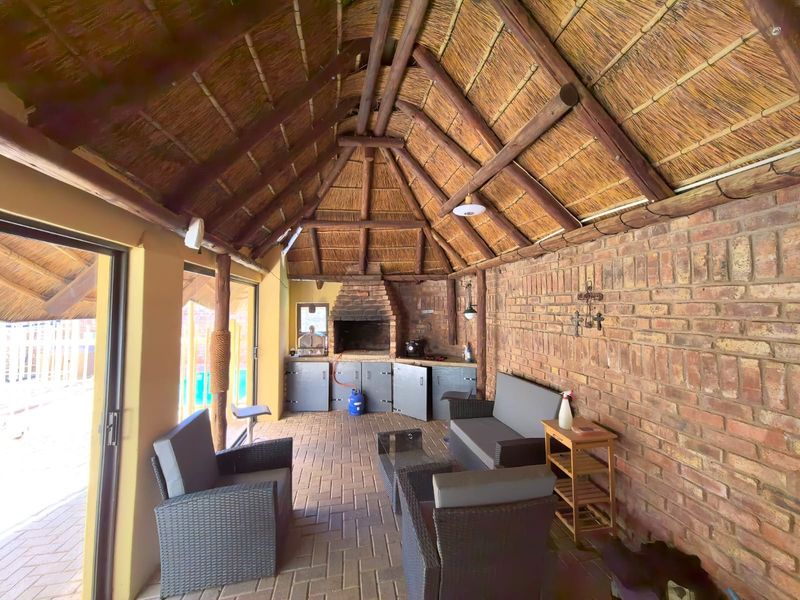 Covered patio area featuring a traditional thatched roof, exposed timber rafters, and a built-in brick braai, perfect for outdoor entertaining.