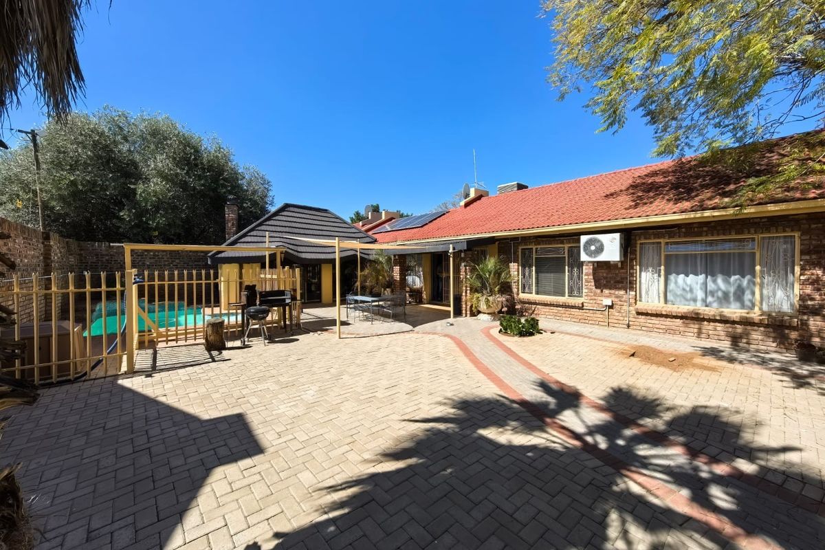 Rear exterior view featuring a paved courtyard, swimming pool, brick facade, and covered patio area under a tiled roof.