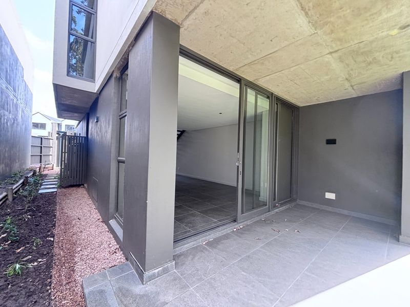A modern covered patio featuring tiled flooring, exposed concrete ceiling, and large sliding glass doors providing seamless access to the interior living space.
