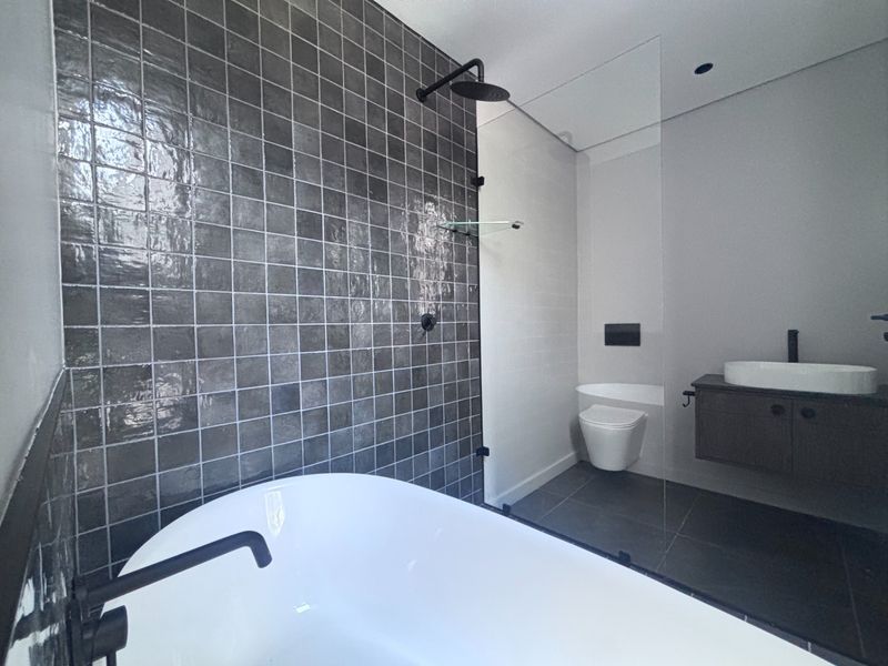 Modern bathroom featuring a freestanding bathtub, glass-enclosed shower, wall-hung toilet, and a sleek vanity with a countertop basin and dark tiled feature wall.