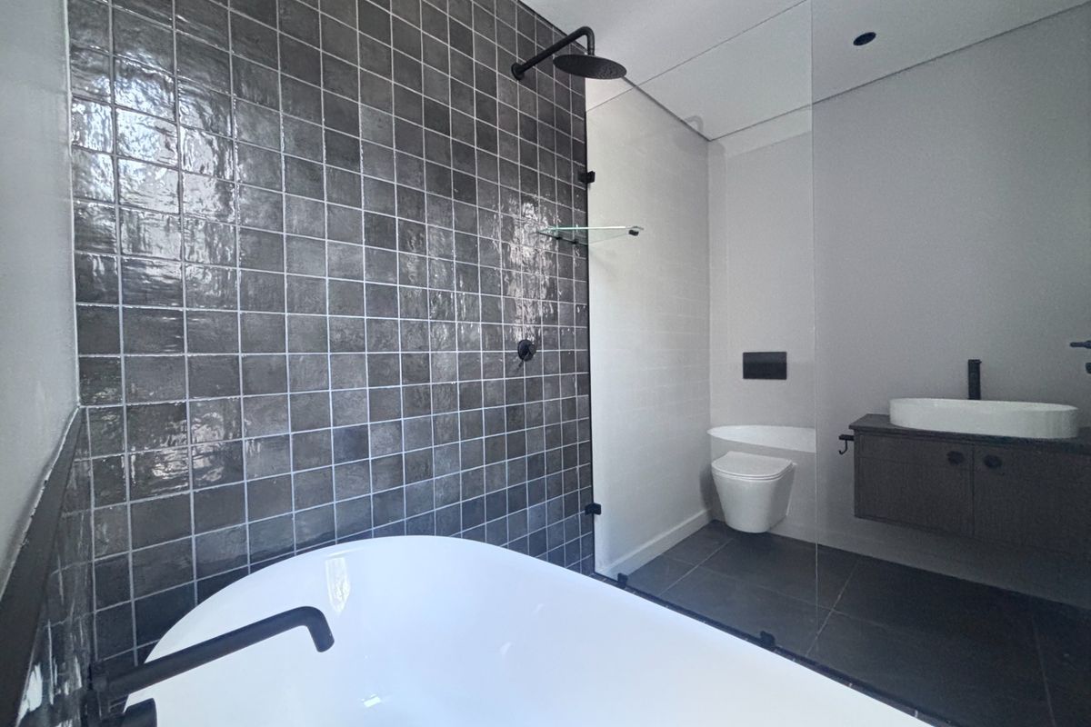 Modern bathroom featuring a freestanding bathtub, glass-enclosed shower, wall-hung toilet, and a sleek vanity with a countertop basin and dark tiled feature wall.