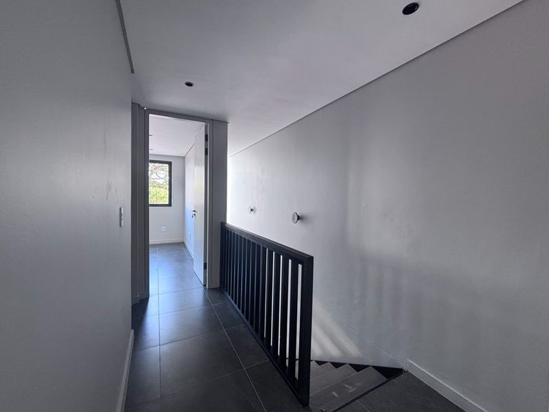 A modern, minimalist hallway featuring dark tiled flooring, a sleek black metal balustrade overlooking the staircase, and recessed ceiling lighting.