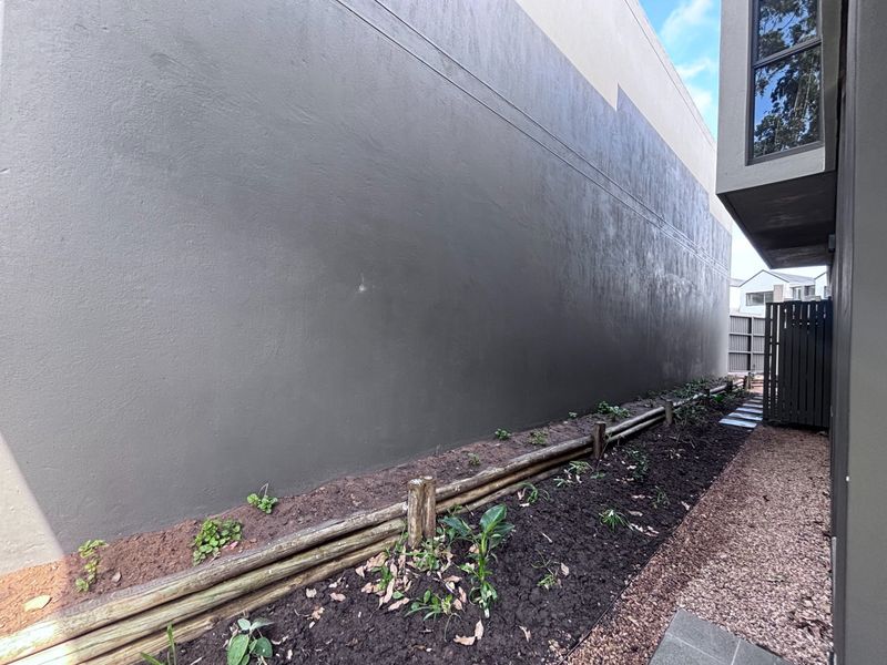A side exterior passage featuring a painted masonry wall, gravel pathway, and timber-edged garden bed.