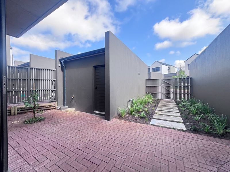 A private rear courtyard featuring brick paving, stone stepping stones, and timber slat fencing, providing a clean and low-maintenance outdoor space.