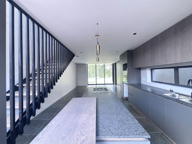 Modern open-plan kitchen featuring a large island with a gas hob, sleek cabinetry, and a striking staircase, leading to a bright living area.