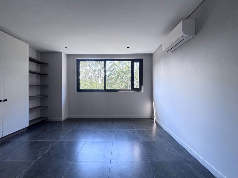 A modern, empty bedroom featuring dark tiled flooring, built-in cupboards with open shelving, and a wall-mounted split-system air conditioner.