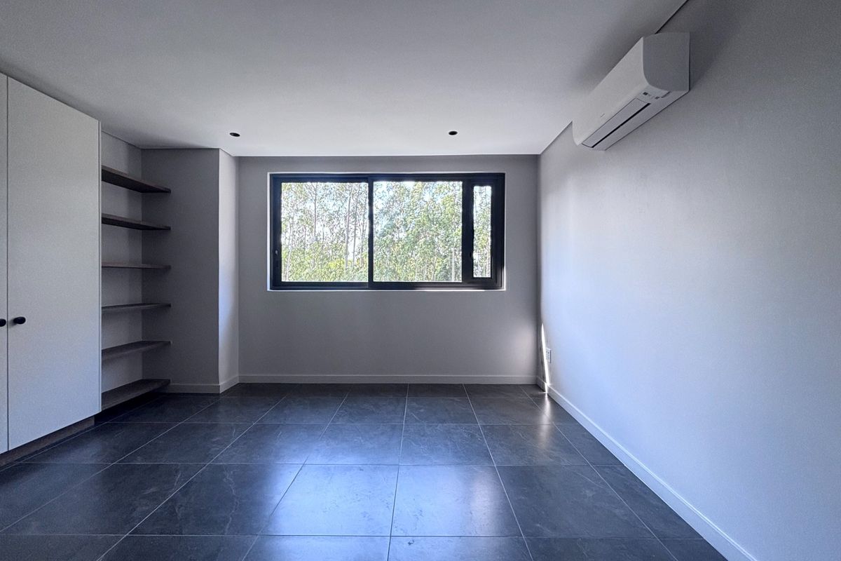 A modern, empty bedroom featuring dark tiled flooring, built-in cupboards with open shelving, and a wall-mounted split-system air conditioner.