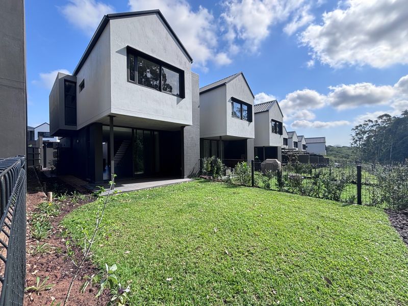 Rear view of modern townhouse units featuring contemporary architectural design, covered patios, and private garden spaces with well-maintained lawns.