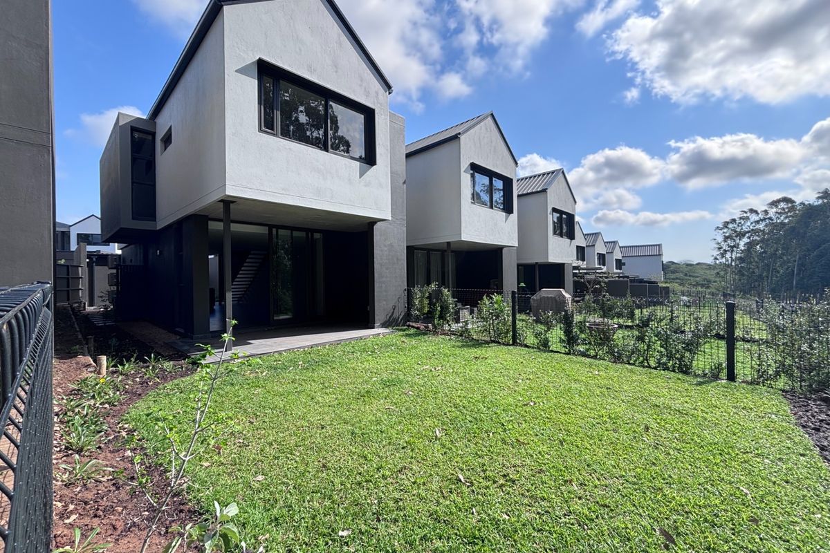 Rear view of modern townhouse units featuring contemporary architectural design, covered patios, and private garden spaces with well-maintained lawns.