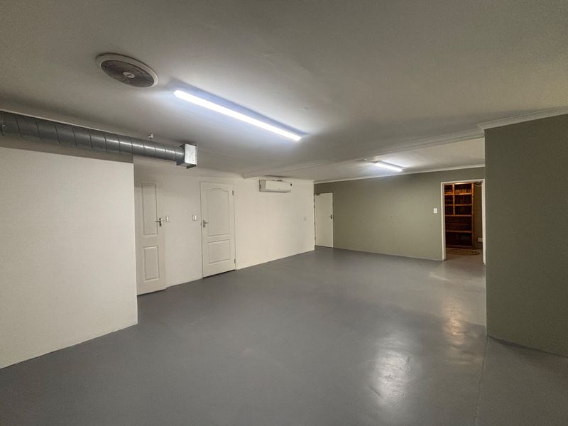 A spacious, clean utility area featuring painted concrete floors, exposed ducting, and split-system air conditioning, suitable for various commercial or storage purposes.