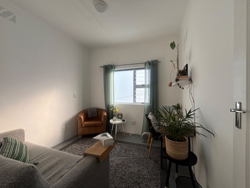 A compact, well-lit living area featuring neutral walls, a functional window with curtains, and standard electrical fixtures.