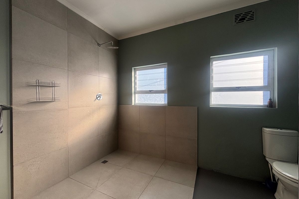 A clean, modern bathroom featuring a spacious walk-in shower with large format tiling, a toilet, and dual louver windows for natural light and ventilation.