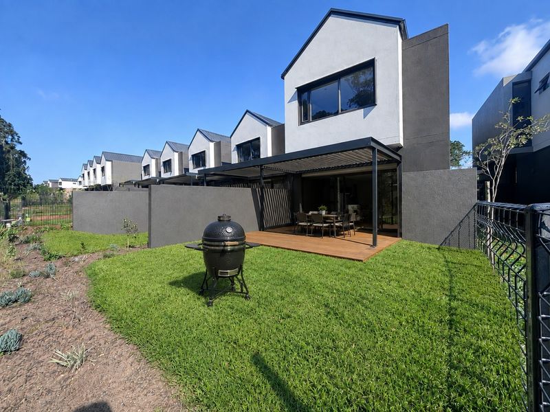 Rear view of a modern townhouse featuring a timber deck, covered patio with louvred roof, and a private landscaped garden.