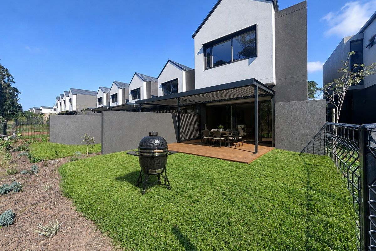 Rear view of a modern townhouse featuring a timber deck, covered patio with louvred roof, and a private landscaped garden.