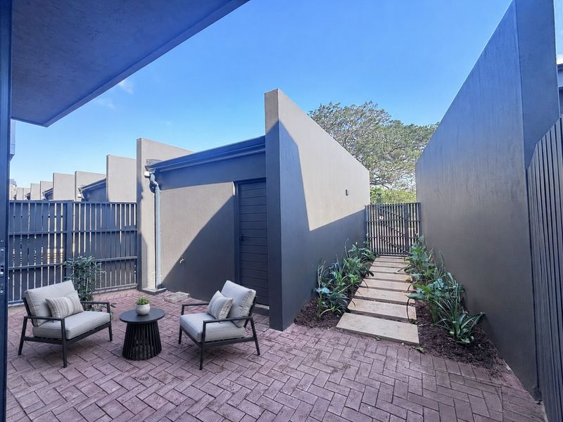 A private, modern paved courtyard featuring high boundary walls, slatted privacy fencing, and a stone pathway leading to an external door.