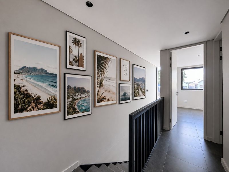 A modern, well-lit hallway featuring tiled flooring, a sleek metal balustrade, and recessed ceiling lighting, leading into an adjacent room.