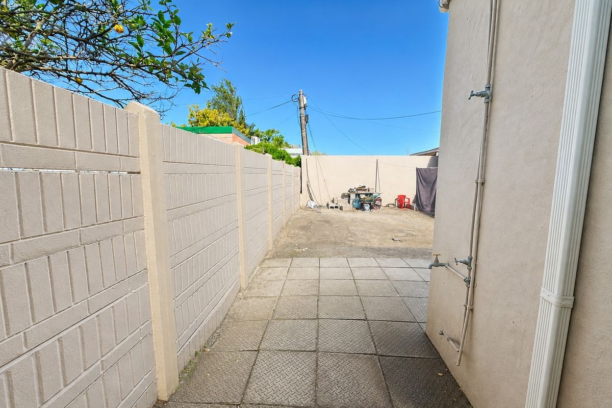 A side yard area featuring a paved walkway, precast concrete boundary wall, and external water taps along the building exterior.
