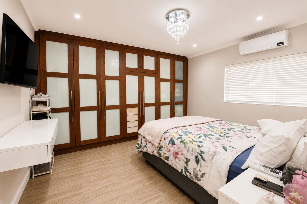 A well-maintained bedroom featuring extensive built-in cabinetry with frosted glass panels, split-system air conditioning, and modern recessed lighting.