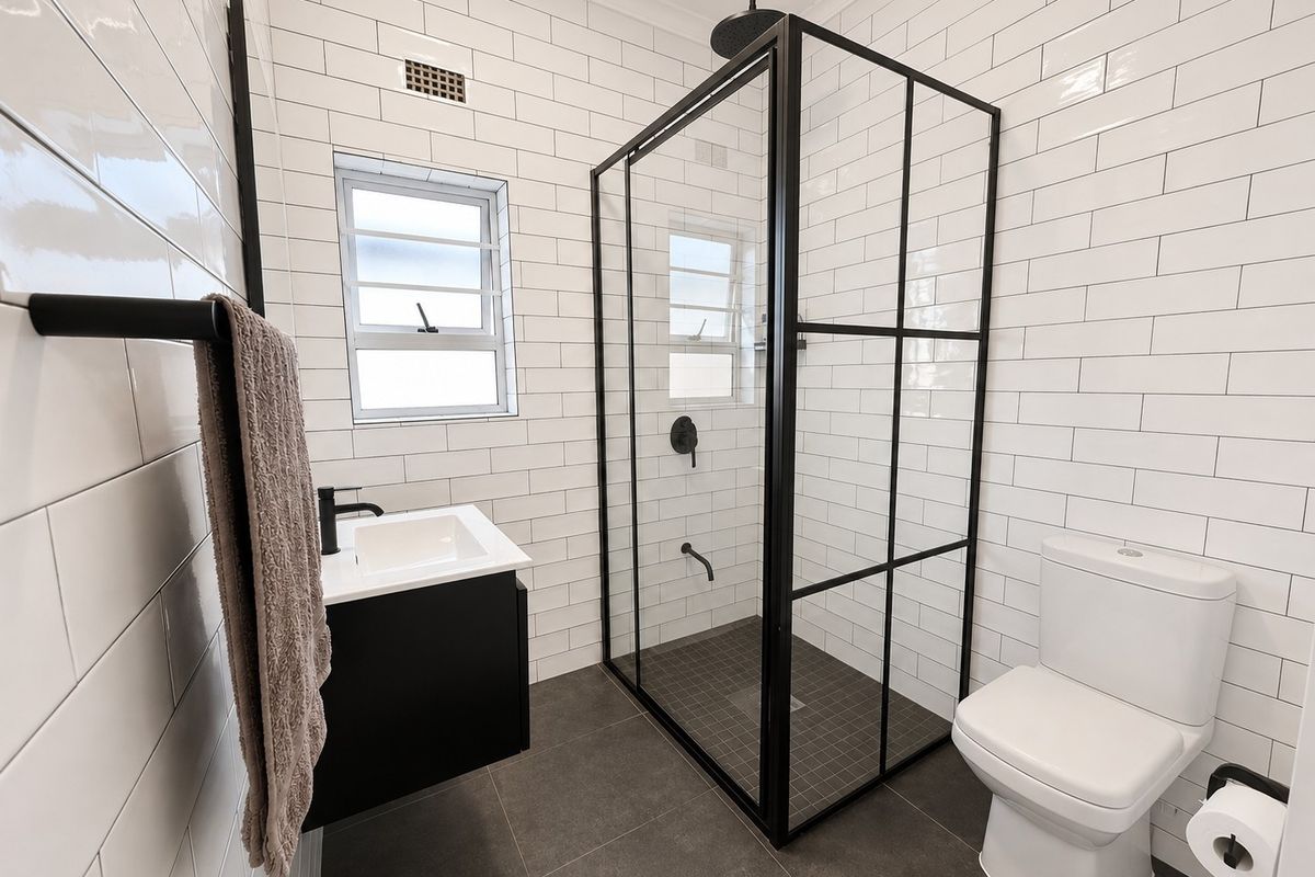Modern renovated bathroom featuring a walk-in shower with black-framed glass, subway wall tiling, dark floor tiles, and a sleek wall-mounted vanity.