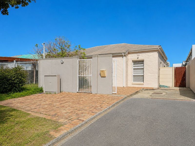 Front exterior view of the property featuring a paved driveway, secure boundary wall with gate, and a tiled roof facade.