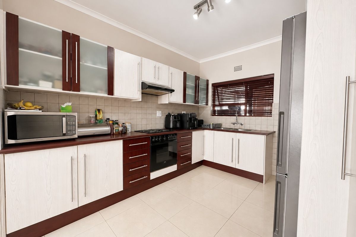 A well-maintained kitchen featuring two-tone cabinetry, tiled backsplash, built-in oven with gas hob, and neutral floor tiles.