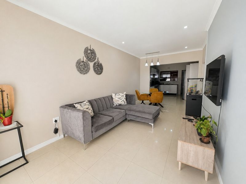 An open-plan living and dining area featuring neutral tiled flooring, recessed lighting, and a seamless transition into a modern kitchen space.
