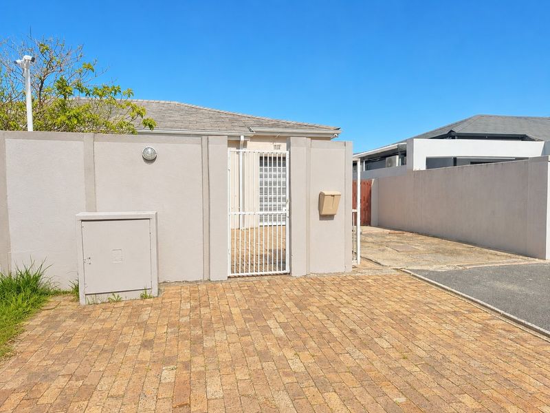 Front exterior view featuring a paved driveway, secure gated entrance, perimeter wall, and integrated utility fixtures.
