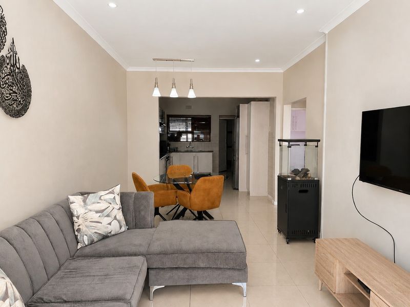 An open-plan living and dining area featuring neutral walls, tiled flooring, recessed lighting, and a view into the adjacent kitchen space.