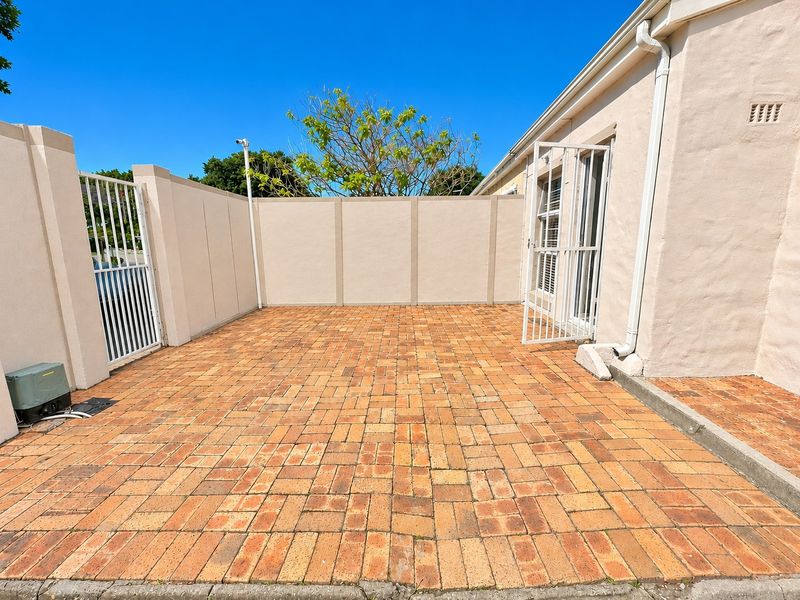A paved outdoor patio area enclosed by boundary walls and a security gate, featuring a clean, well-maintained brick surface.